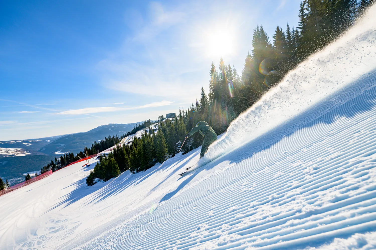 En skiløper suser ned en snødekt bakke i solskinn på Kvitfjell. Skogkledde åser i bakgrunnen.