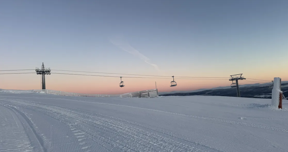 Skitrekk på et snødekt fjell i soloppgang, med pastellfarget himmel i bakgrunnen.