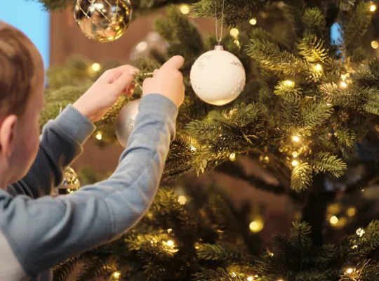 Gutt som henger opp julekule på treet. 